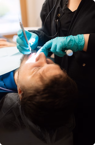Dentist in black attire and green gloves examines a patient’s mouth with tools. The patient appears relaxed, conveying a routine dental check-up.